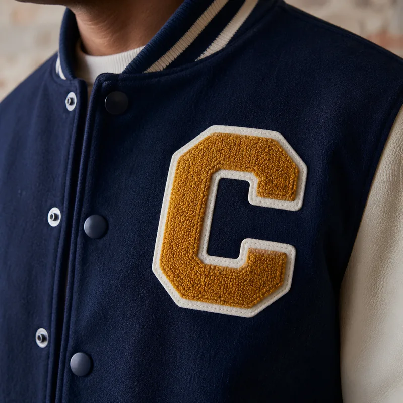 Gold chenille letter C with cream border on a navy leather-sleeve varsity jacket